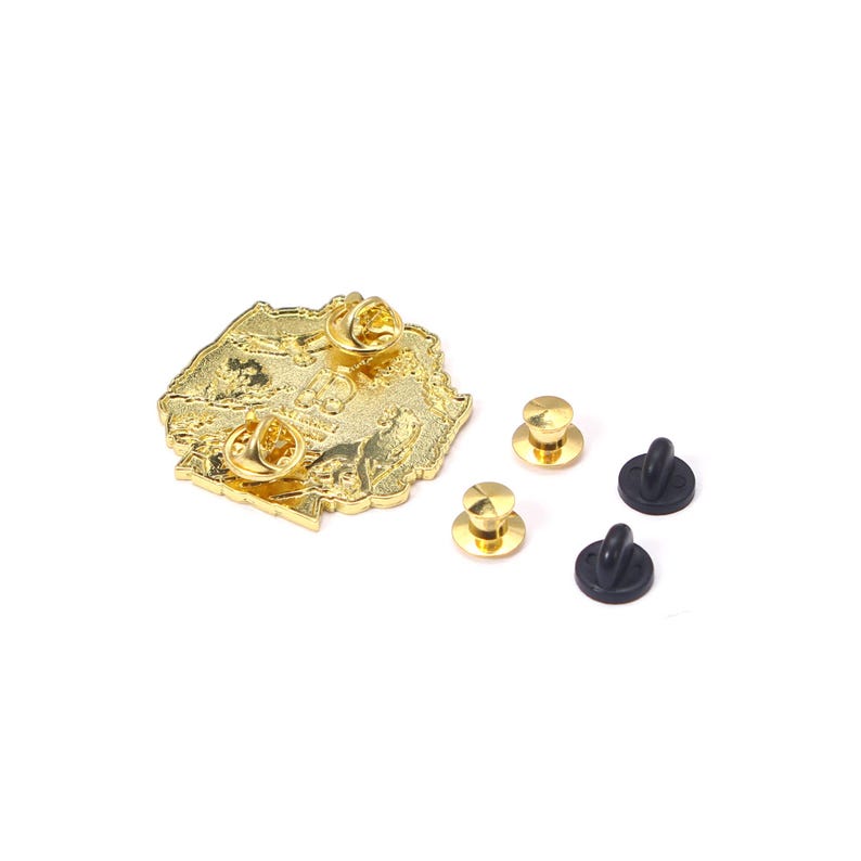 May include: A gold-colored pin in the shape of a map, with a detailed design. The pin has two pin backs attached, with three additional gold-colored pin backs and two black rubber clasps. The pin is on a white background.