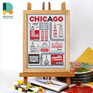 Puede incluir: Una obra de arte en punto de cruz enmarcada de los monumentos de Chicago, incluyendo rascacielos y una bicicleta, en rojo, negro y gris. La palabra "CHICAGO" está en la parte superior. La obra de arte se exhibe en un caballete de madera.