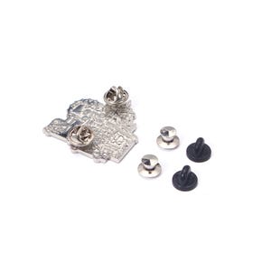 Op de afbeelding: Een zilverkleurige metalen pin met een gedetailleerd ontwerp, mogelijk een bezienswaardigheid of stadsgezicht, en twee pinruggen. Drie extra pinruggen, twee zilverkleurige en twee zwarte, zijn ook zichtbaar. De pin staat op een witte achtergrond.