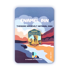 May include: An enamel pin depicting a landscape of Theodore Roosevelt National Park. The pin is presented on a card with the text "ENAMEL PIN" and "THEODORE ROOSEVELT NATIONAL PARK". The pin has a gold border and a colourful landscape.