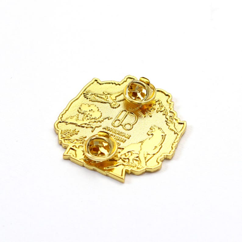 May include: A gold-colored metal pin with a detailed design featuring an eagle, a wolf, and the text "Awesome Western". The pin has two pin backs for secure attachment and is likely a collectible or souvenir item.