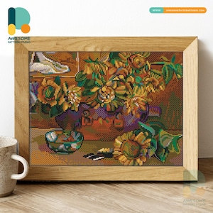 Könnte beinhalten: Ein gerahmtes Kreuzstich-Kunstwerk mit einem Stillleben aus Sonnenblumen und anderen Blumen in einer Vase. Das Kunstwerk hat einen Holzrahmen und wird auf einer Holzoberfläche präsentiert. Die Farbpalette umfasst Gelb-, Grün-, Orange- und Lilatöne.
