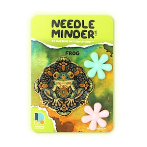 May include: A needle minder featuring a frog with a colorful mandala design. The minder comes with two magnetic flower-shaped needle holders, one in light blue and one in pink.