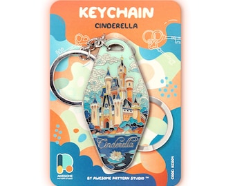 May include: A motel-style keyring featuring a colourful illustration of a castle with blue, orange, and cream accents. The keyring is attached to a silver metal ring and mounted on a backing card labelled KEYCHAIN CINDERELLA by AWESOME PATTERN STUDIO.