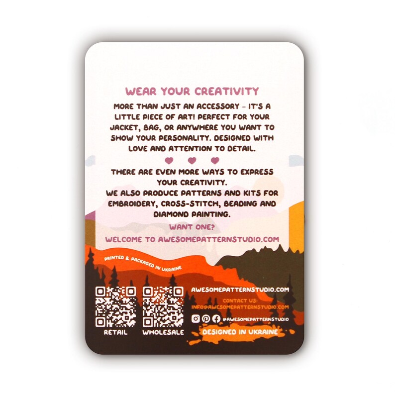 May include: A rectangular card with rounded corners, featuring text that reads "WEAR YOUR CREATIVITY." The card has a landscape design with a forest silhouette and text promoting patterns and kits for embroidery, cross-stitch, beading, and diamond painting.