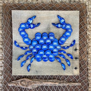 May include: A blue crab made from Bud Light bottle caps on a wooden background. The crab is made with the bottle caps forming the body and claws.