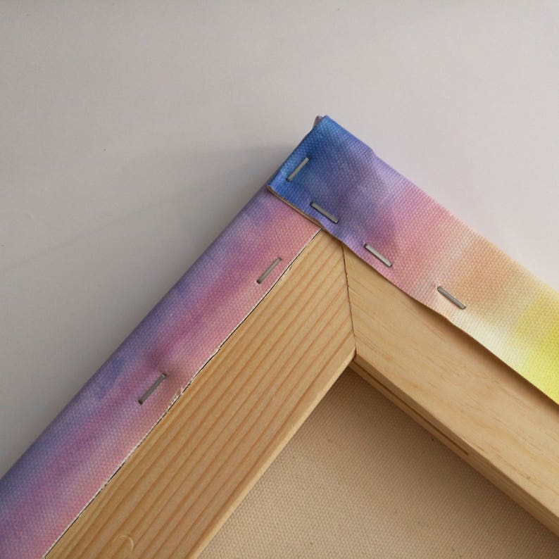 May include: Close-up of a corner of a wooden canvas frame with a colorful ombre fabric stretched over it. The fabric is secured with staples.