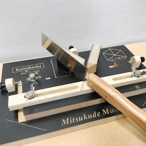 Puede incluir: Un jig de madera para trabajar la madera con una hoja de sierra y un mango. El jig está etiquetado como "kumiko4u" y "Mitsukude Mas".