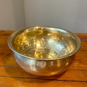 May include: A hammered brass bowl with a shiny gold finish. The bowl is round and has a slightly flared rim.