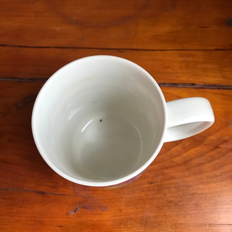 May include: White ceramic mug with a handle. The mug is empty and has a small black dot on the inside.