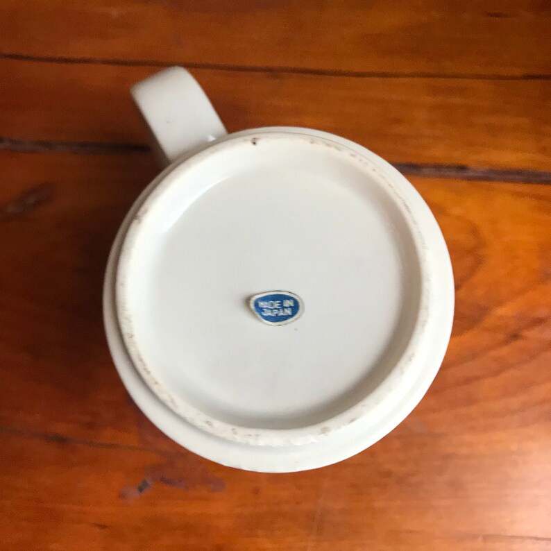May include: White ceramic mug with a blue and white "Made in Japan" sticker on the bottom.
