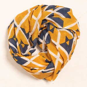 K&ouml;nnte beinhalten: Senfgelber Infinity-Schal mit einem geometrischen Muster in Marineblau und Wei&szlig;. Der Schal ist aus einem weichen, leichten Stoff gefertigt und ist als Schlaufe um den Hals konzipiert. Ein stilvolles Accessoire f&uuml;r jedes Outfit.
