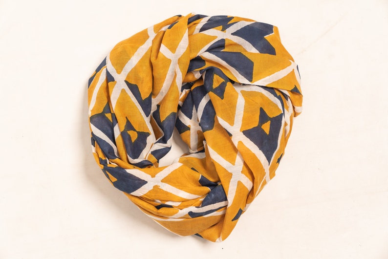 K&ouml;nnte beinhalten: Senfgelber Infinity-Schal mit einem geometrischen Muster in Marineblau und Wei&szlig;. Der Schal ist aus einem weichen, leichten Stoff gefertigt und ist als Schlaufe um den Hals konzipiert. Ein stilvolles Accessoire f&uuml;r jedes Outfit.