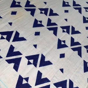 K&ouml;nnte beinhalten: Wei&szlig;er Stoff mit einem sich wiederholenden Muster aus dunkelblauen geometrischen Formen. Das Design zeigt Dreiecke und Quadrate, die diagonal angeordnet sind und eine moderne &Auml;sthetik erzeugen. Der Stoff scheint leicht zu sein.