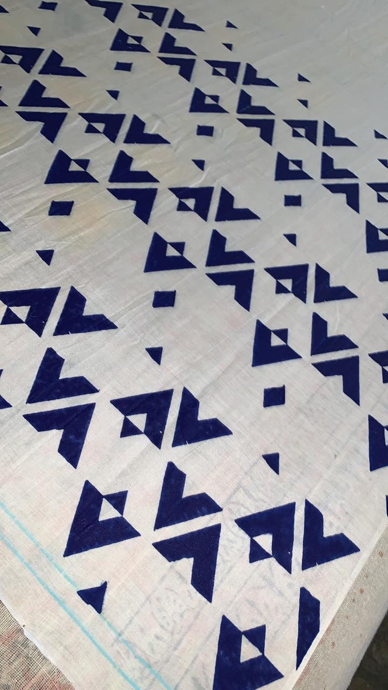 K&ouml;nnte beinhalten: Wei&szlig;er Stoff mit einem sich wiederholenden Muster aus dunkelblauen geometrischen Formen. Das Design zeigt Dreiecke und Quadrate, die diagonal angeordnet sind und eine moderne &Auml;sthetik erzeugen. Der Stoff scheint leicht zu sein.