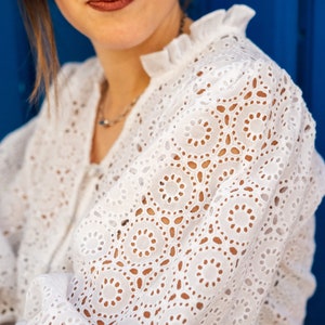 K&ouml;nnte beinhalten: Wei&szlig;e Blusenbluse mit R&uuml;schenkragen. Die Bluse hat ein zartes Muster aus kleinen Kreisen und Ovalen.