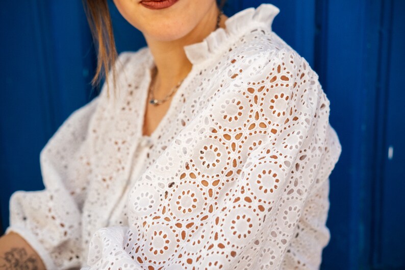 K&ouml;nnte beinhalten: Wei&szlig;e Blusenbluse mit R&uuml;schenkragen. Die Bluse hat ein zartes Muster aus kleinen Kreisen und Ovalen.
