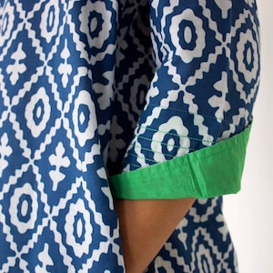 May include: A blue and white patterned garment with a geometric design. The sleeve cuff is a solid green colour. The fabric appears to be cotton or a similar material. The garment is likely a tunic or dress.