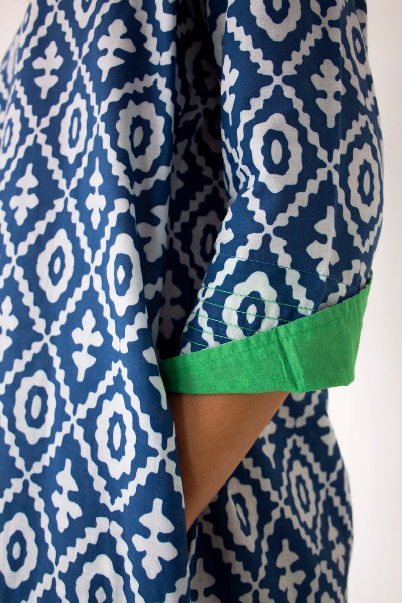 May include: A blue and white patterned garment with a geometric design. The sleeve cuff is a solid green colour. The fabric appears to be cotton or a similar material. The garment is likely a tunic or dress.