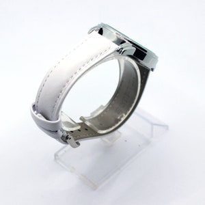 May include: A silver wristwatch with a white leather band. The watch face is not visible in the image.