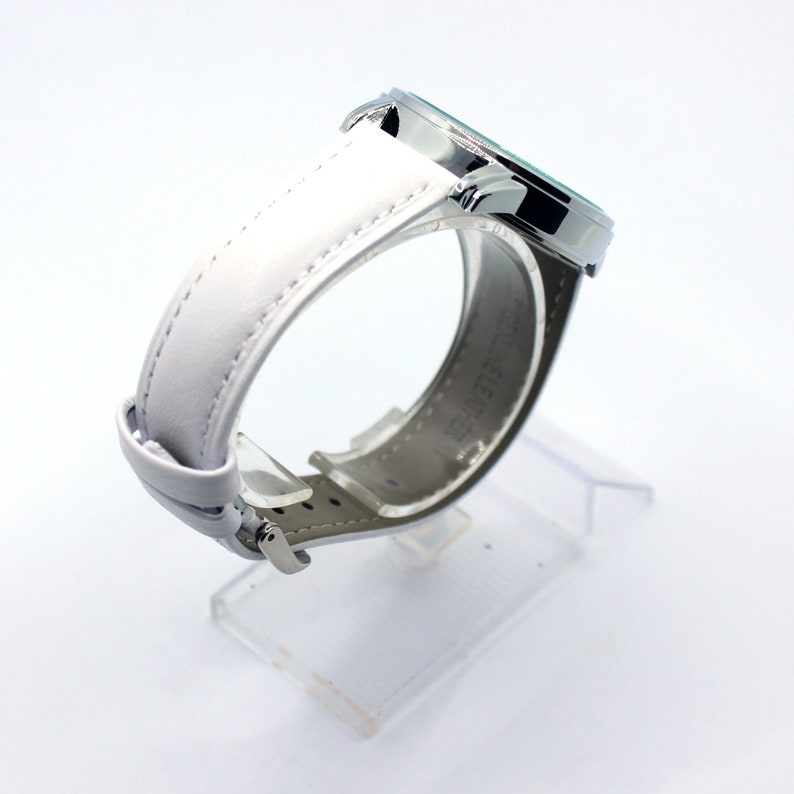 May include: A silver wristwatch with a white leather band. The watch face is not visible in the image.