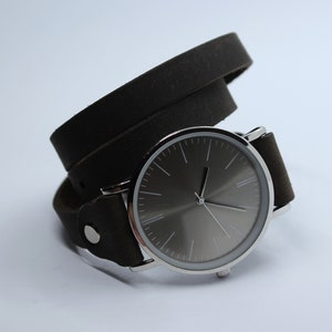 Peut inclure: Une montre argent&eacute;e avec un cadran gris fonc&eacute; et un bracelet en cuir noir. Le bracelet est enroul&eacute; deux fois autour de la montre.
