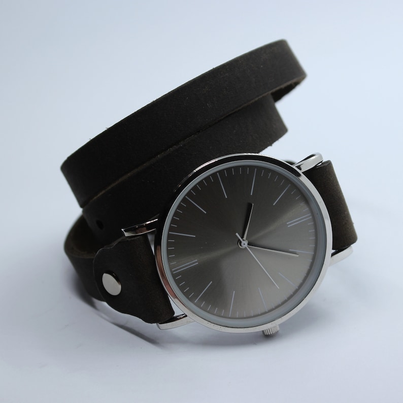 Peut inclure: Une montre argent&eacute;e avec un cadran gris fonc&eacute; et un bracelet en cuir noir. Le bracelet est enroul&eacute; deux fois autour de la montre.