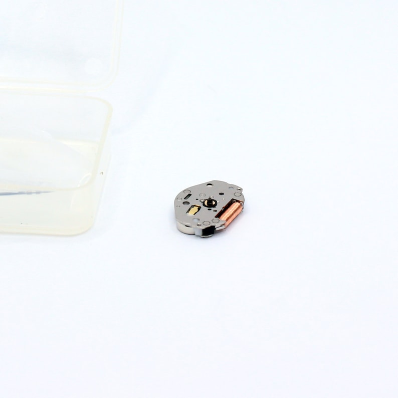 May include: A silver watch movement with a copper winding stem. The movement is designed for a quartz watch.