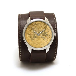 Puede incluir: Un reloj de pulsera de cuero marrón con caja plateada y esfera con mapa del mundo.