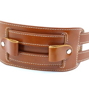 May include: A brown leather watch band with white stitching and silver buckles. The band has a pocket on the front with a flap.