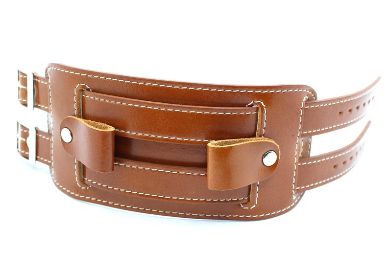 May include: A brown leather watch band with white stitching and silver buckles. The band has a pocket on the front with a flap.