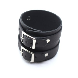 May include: Black leather cuff bracelet with two silver buckles. The cuff is adjustable and has a simple design.
