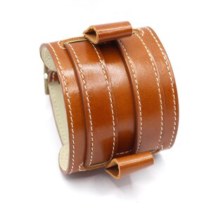 May include: A brown leather watch band with white stitching. The band has a buckle closure and is designed to fit a wrist.