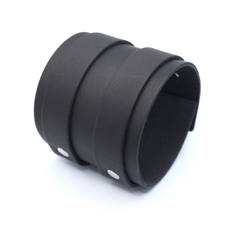 May include: A black leather cuff bracelet with silver metal accents. The bracelet is made of multiple layers of leather and has a simple, minimalist design.