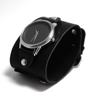 May include: A black leather cuff watch with a silver face and black hands.