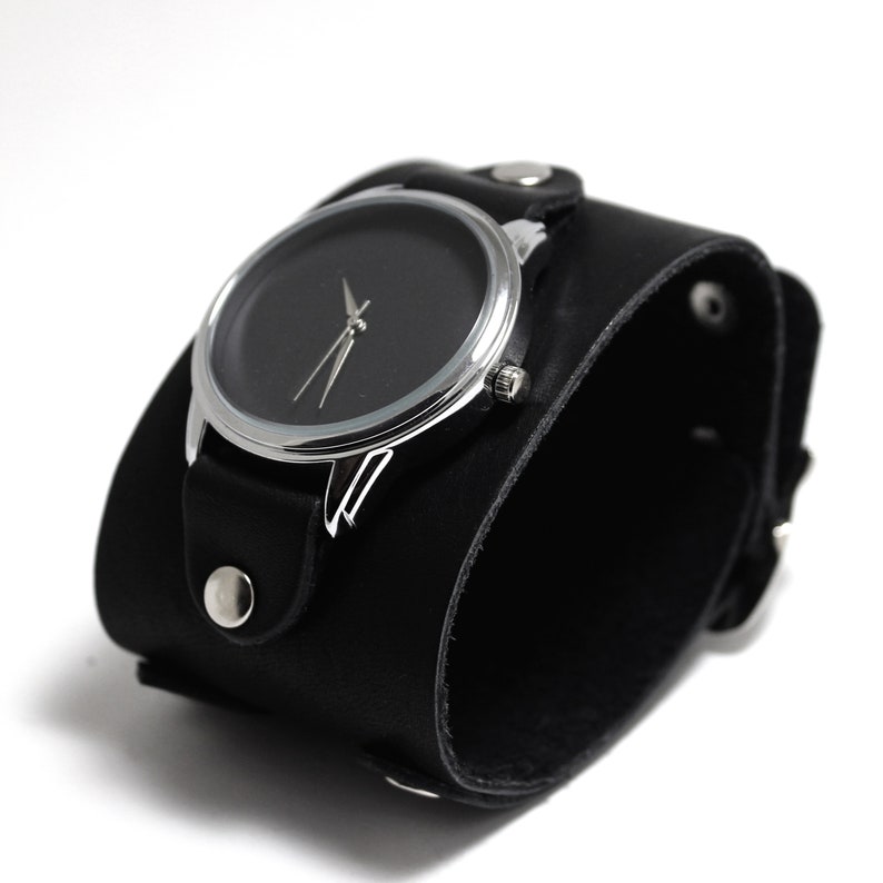 May include: A black leather cuff watch with a silver face and black hands.