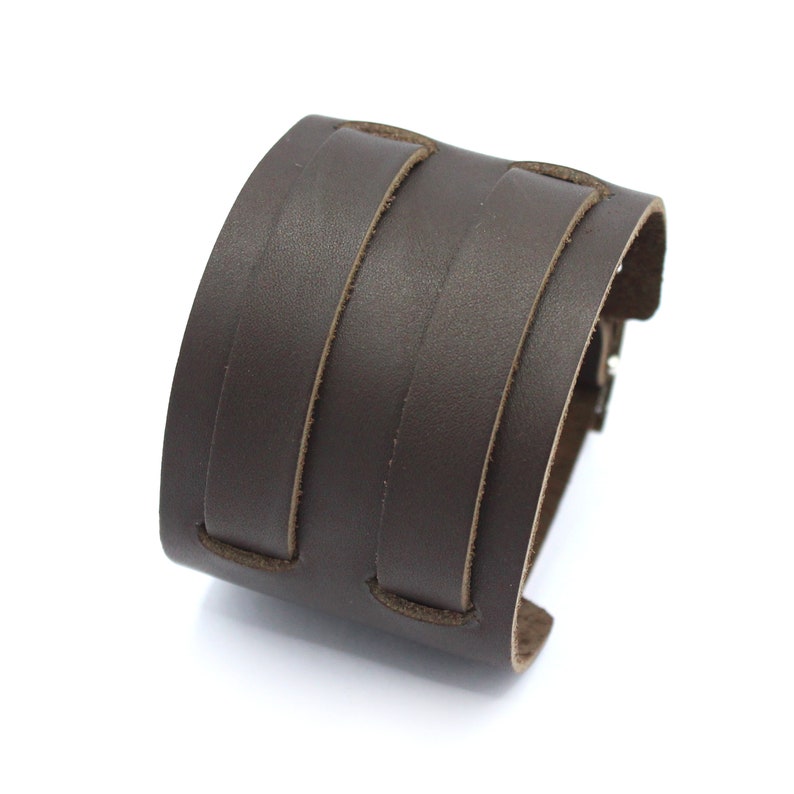 May include: A brown leather cuff bracelet with two stitched bands.