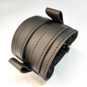 May include: Black leather cuff bracelet with a buckle closure and multiple stitched layers.
