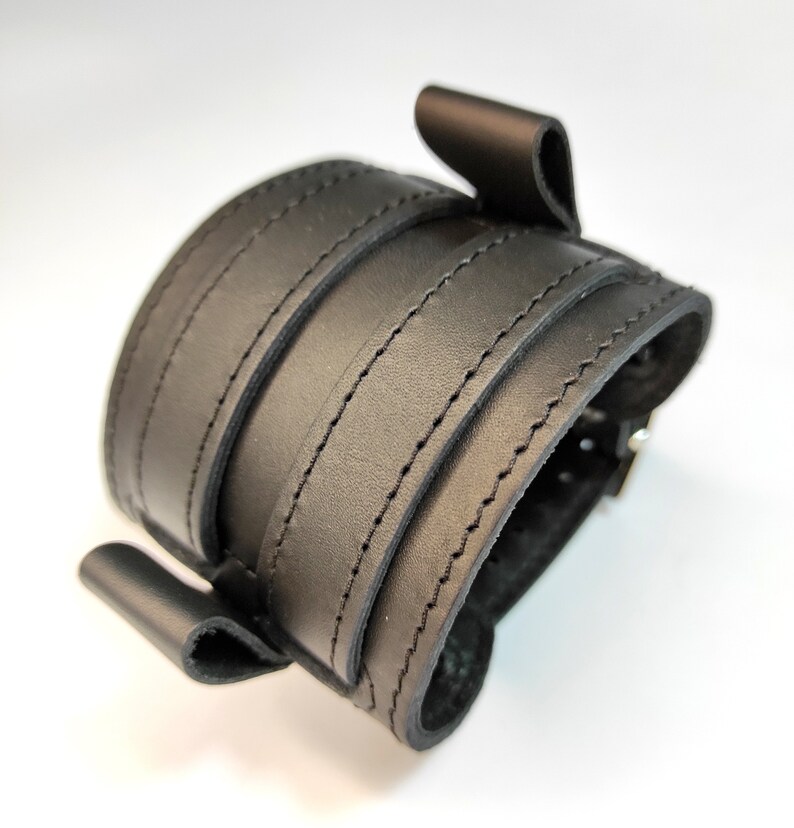 May include: Black leather cuff bracelet with a buckle closure and multiple stitched layers.
