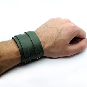 May include: A dark green leather cuff bracelet with a simple design. The bracelet is adjustable and has a metal clasp.