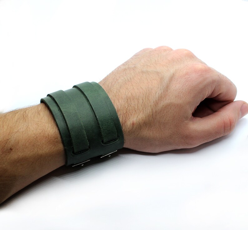 May include: A dark green leather cuff bracelet with a simple design. The bracelet is adjustable and has a metal clasp.