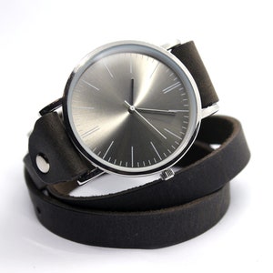 Peut inclure: Une montre argent&eacute;e avec un cadran gris et un bracelet en cuir noir. Le bracelet est enroul&eacute; deux fois autour de la montre.