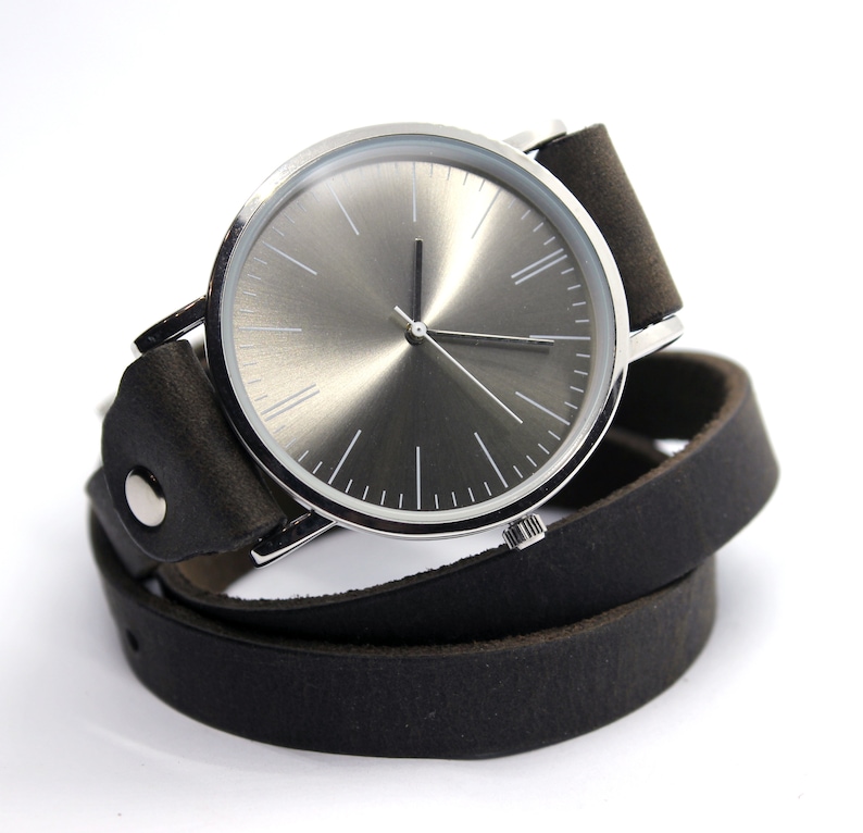 Peut inclure: Une montre argent&eacute;e avec un cadran gris et un bracelet en cuir noir. Le bracelet est enroul&eacute; deux fois autour de la montre.