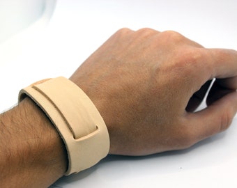 May include: A light brown leather bracelet with a simple design. The bracelet is adjustable and has a buckle closure.