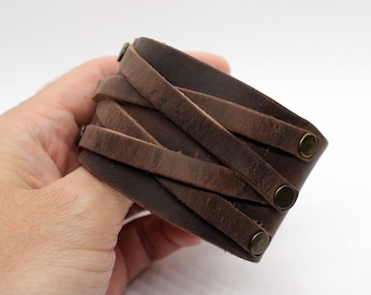 May include: A brown leather cuff bracelet with a woven design and brass accents.
