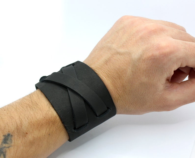 May include: A black leather bracelet with a braided design. The bracelet is worn on a person's wrist.