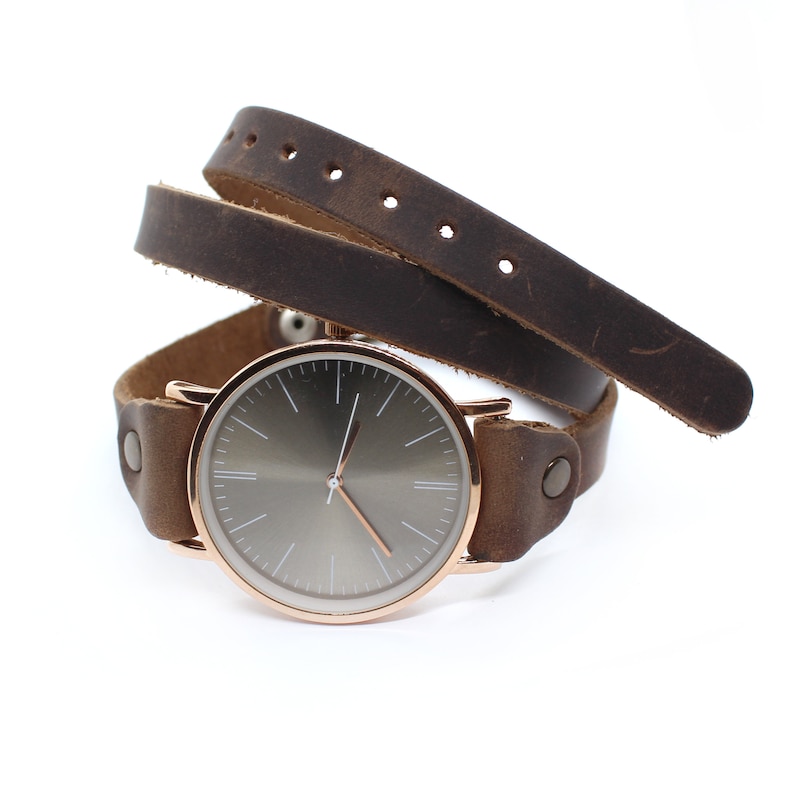 Peut inclure: Une montre en or rose avec un cadran gris fonc&eacute; et un bracelet en cuir marron. Le bracelet est enroul&eacute; deux fois autour de la montre.
