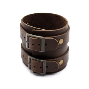 May include: A brown leather cuff bracelet with two adjustable buckles and brass accents.
