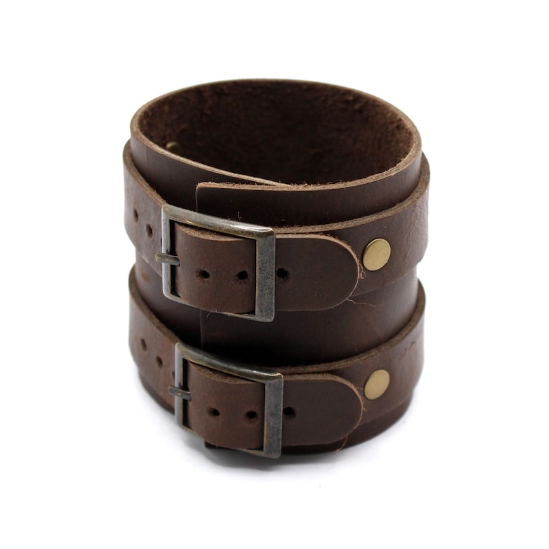 May include: A brown leather cuff bracelet with two adjustable buckles and brass accents.