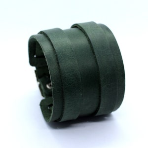 May include: A dark green leather cuff bracelet with multiple layers of leather. The bracelet has a silver buckle and stitching.